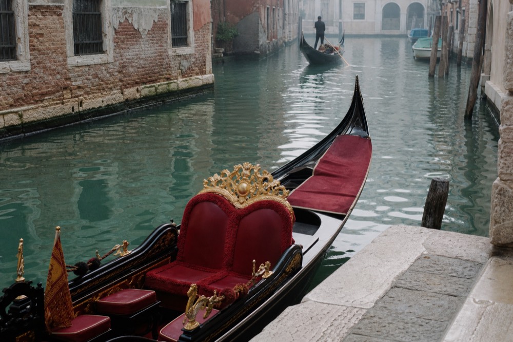 An empty gondola bench upholstered in deep red velvet with brass trim, photographed from above at the mooring