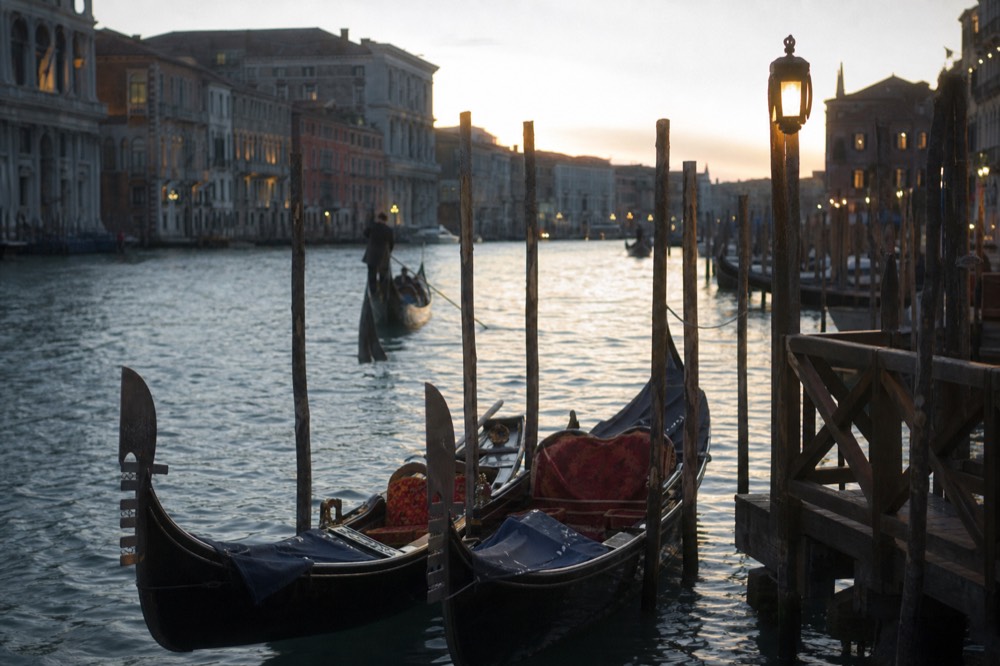 Two gondolas moored side by side at a wooden landing stage on a wide canal, low winter sun striking the water