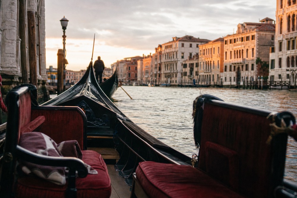 Empty gondola seats facing each other with a folded blanket on one bench, the canal surface bright behind the low black hull