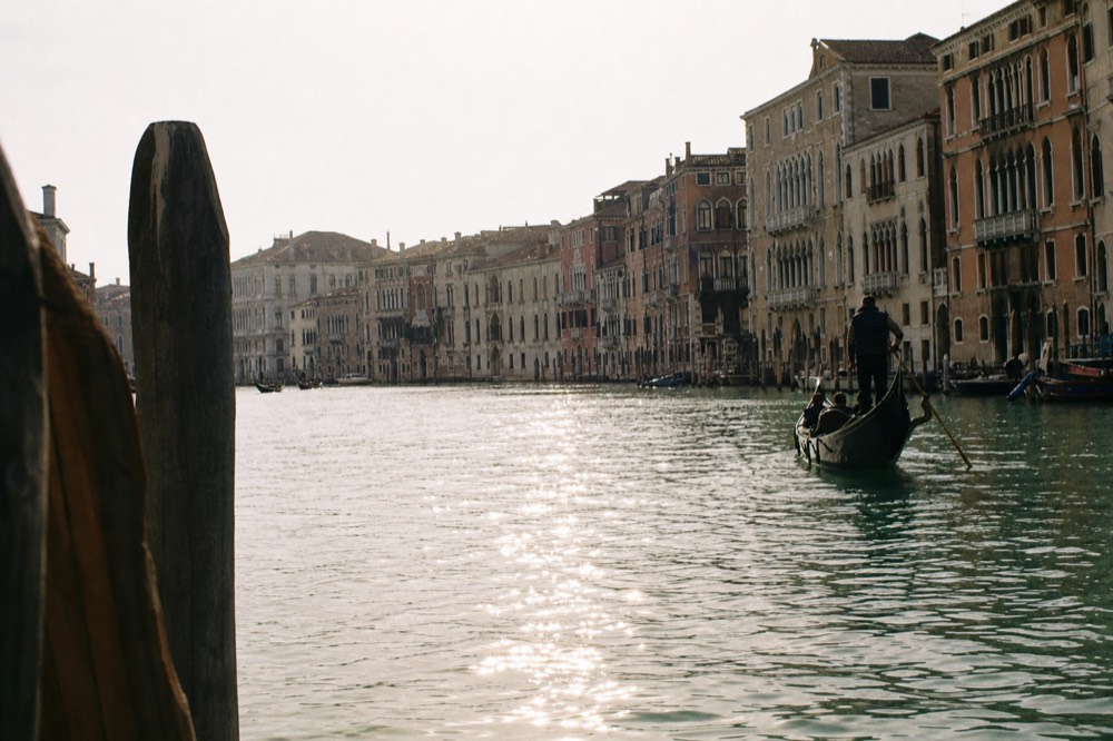 The great bend of a Venetian waterway seen from low on the water, palace facades stacking into the curve under flat afternoon light