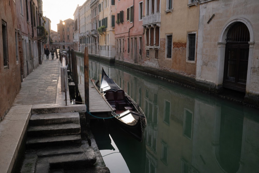 An empty gondola held alongside a low wooden pontoon by a mooring rope, worn steps leading down to the water from a stone pavement