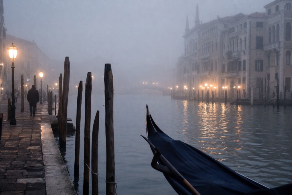 Thick winter fog reducing a Venetian canal to grey shapes, mooring posts fading into white and a bridge barely visible in the distance