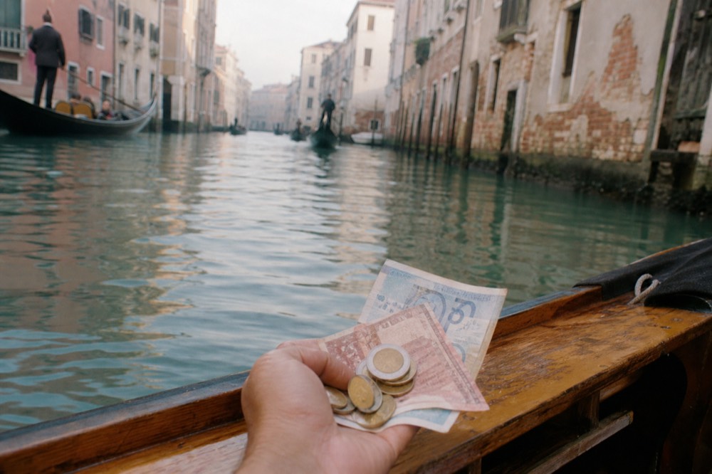 Euro banknotes and coins held in a hand above a wooden boat gunwale with canal water blurred beneath