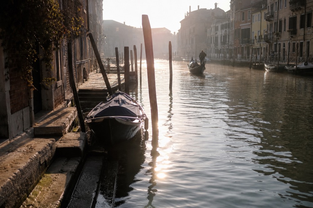 An empty canal at first light with mist over the water and a single moored boat rocking beside worn stone steps
